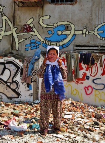 A woman holding a photo of Ny Sokha in a neighborhood filled wit